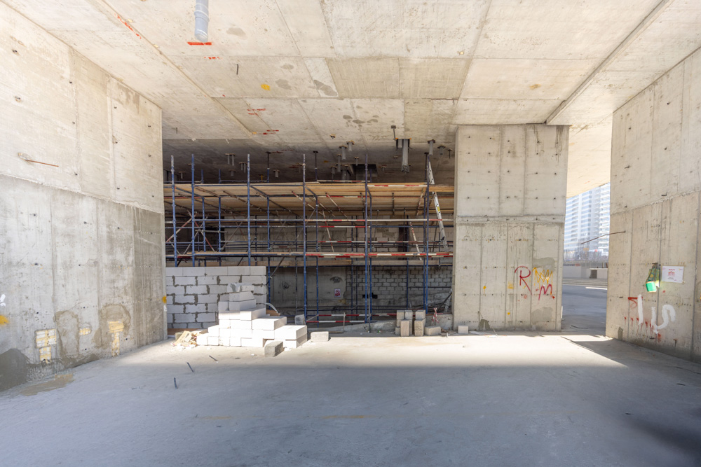 Cove Edition I By Imtiaz 1 An unfinished construction site featuring concrete walls, scaffolding, and stacks of building blocks on the floor.